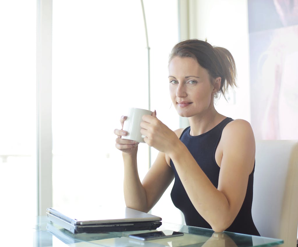 Young woman sitting at her desk, holding a coffee cup and smiling. Ideal for workplace and lifestyle themes.