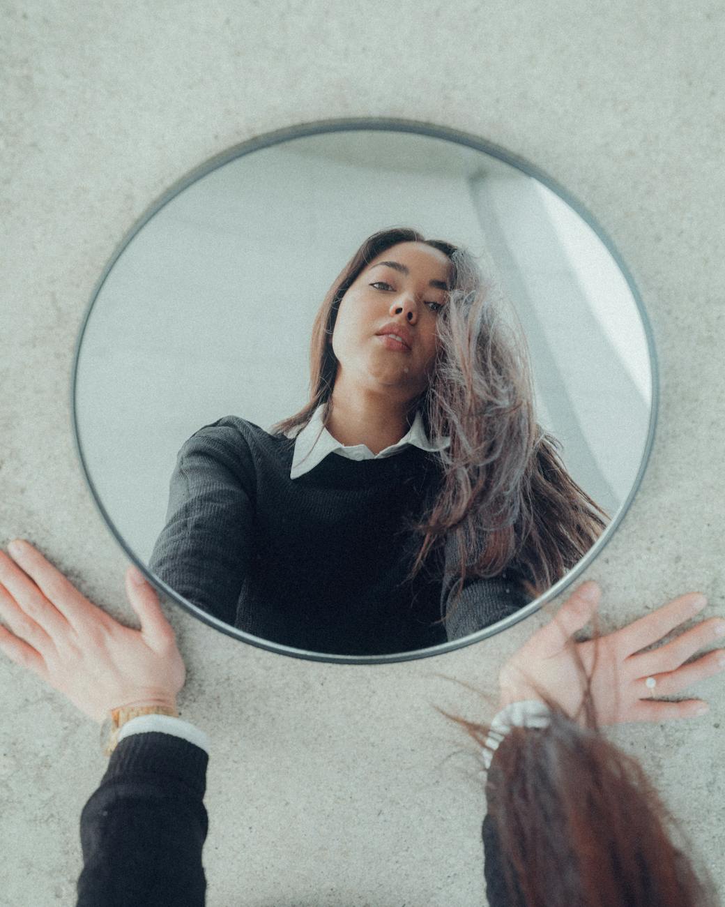 reflection of young woman in black sweater in mirror on floor